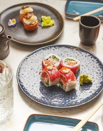 Mesa com pratos de sushi, com um copo de agua e molhos